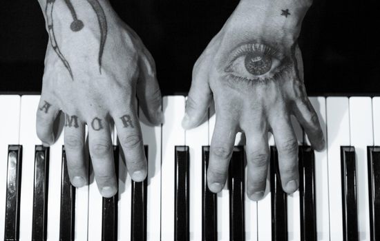 Tattooed mans hands on the keyboard of a piano. Dark background