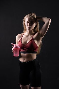 In girl a pink holds hand her spotrsman shaker in black background shaker pink fitness body, for gym woman for healthy and training strength, beautiful wellness. Sweat model beauty, power
