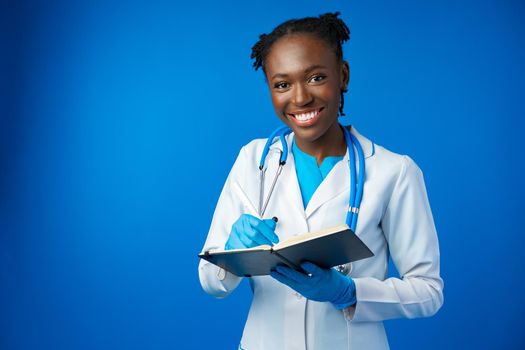 Black female doctor student wearing a lab coat with book in blue studio