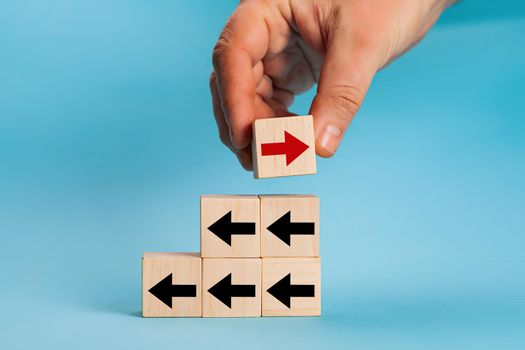 Businessman hand picked wooden block with red arrow facing the opposite direction black arrows, unique, think different, individual and standing out from the crowd concept, technology innovation,