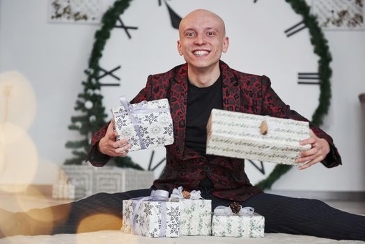 Can't wait to open it. Man with big clock behind him sitting with New year gift boxes in holiday clothings.