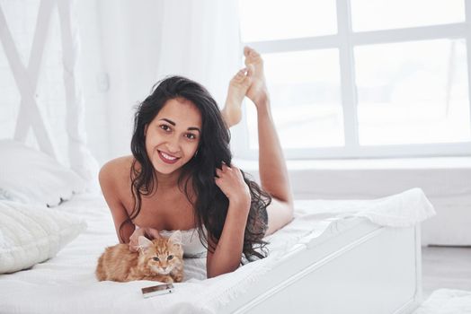 Nice portrait. Attractive blonde resting on the white bed with her cute kitten.