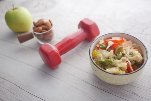 Fitness concept with dumbbell, fresh vegetable , almond and apple on table .