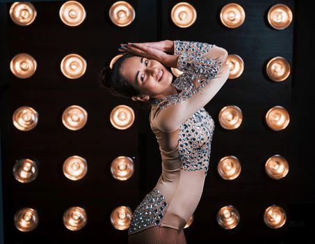 Beautiful female assistant of magician posing in the studio with lights behind her.