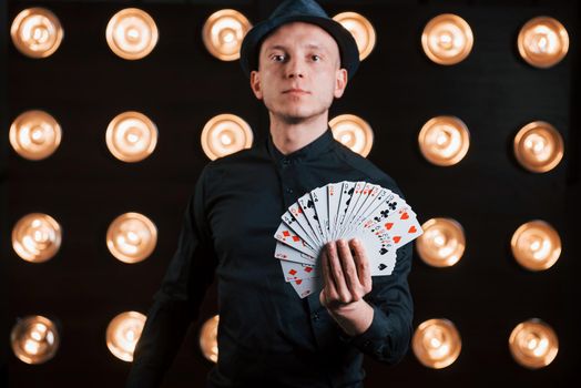 Just pick your card. Magician in black suit standing in the room with special lighting at backstage.