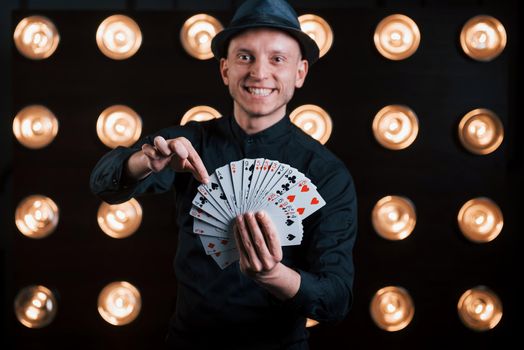 He's takes your card. Magician in black suit standing in the room with special lighting at backstage.