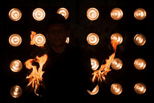 Dangerous beauty of the fire in the hands. Professional magician showing trick. Light bulbs on background.