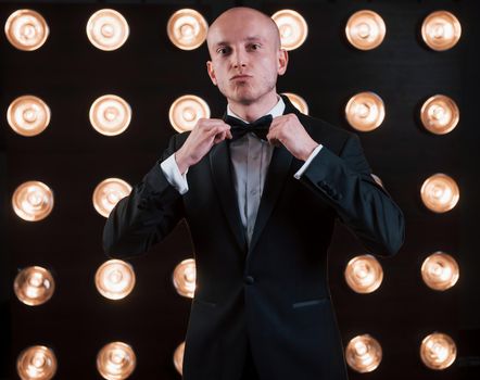 Adjusts the tie. Ready for the show. Magician in black suit standing in the room with special lighting at backstage.