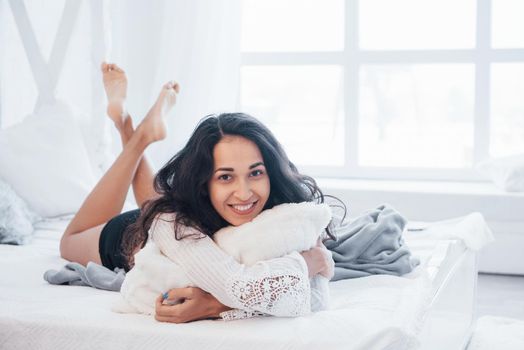 Relaxing at holiday time. Brunette having a rest on the white couch in her bedroom at daytime.