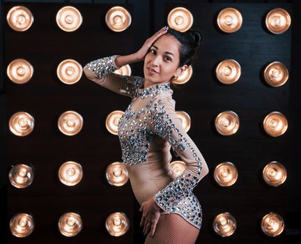 Good slim body. Beautiful female assistant of magician posing in the studio with lights behind her.