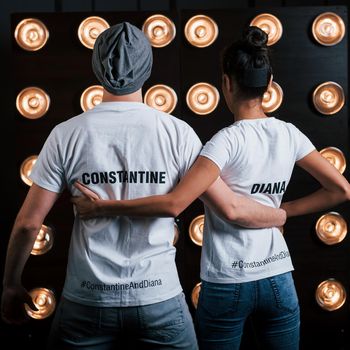 Hugs each other. Back view of couple in shirts with their names on it standing next to studio lights.