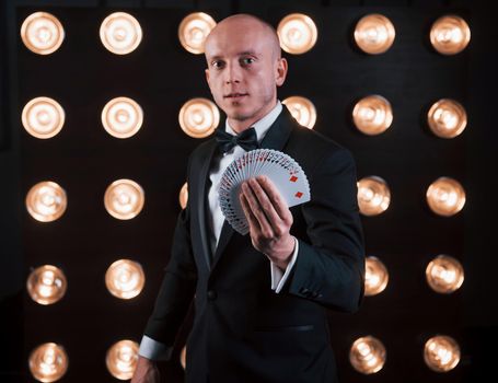 On the work. Magician in black suit standing in the room with special lighting at backstage.