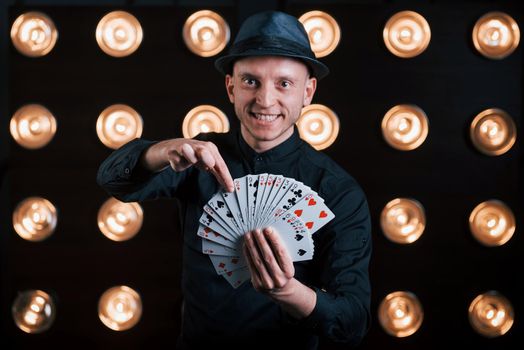 He's gonna guess your card. Magician in black suit standing in the room with special lighting at backstage.