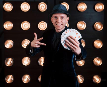 Card tricks in action. Magician in black suit standing in the room with special lighting at backstage.