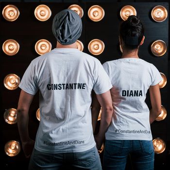 Back view of couple in shirts with their names on it standing next to studio lights.