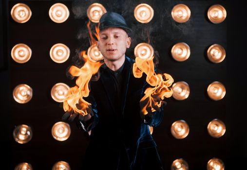 The fire is in his hands. Professional magician showing trick. Light bulbs on background.