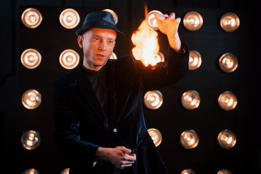 Controlling the flame. Professional magician showing trick. Light bulbs on background.