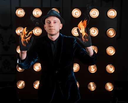 Hands is burning but this is no big deal for this magician. Professional illusionist in black hat, shirt and gloves playing with fire.