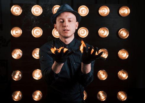 Controlling the burning process. Professional illusionist in black hat, shirt and gloves playing with fire.