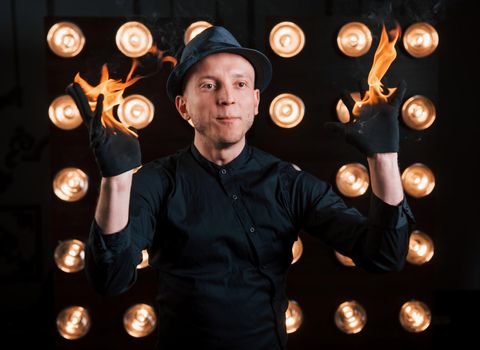 Professional illusionist in black hat, shirt and glowes playing with fire.