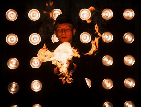 The powers of nature is in good hands. Professional magician showing trick and playing with fire. Light bulbs on background.