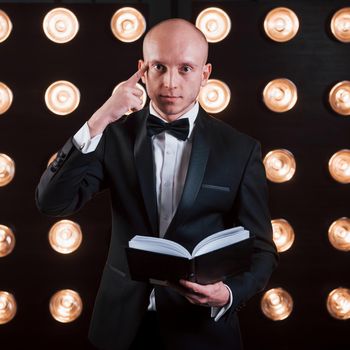 Reading your mind. Magician in black suit standing in the room with special lighting at backstage.