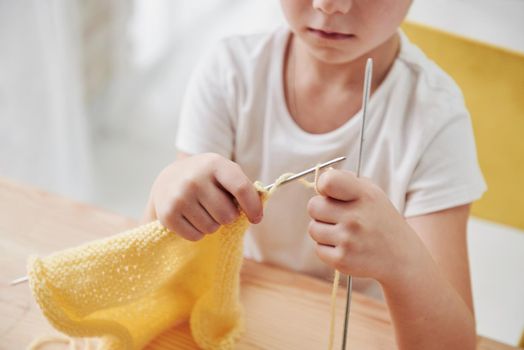 Doing some knots. Kid is knitting at home. Cute little girl sitting near the wooden table is learning some new stuff.