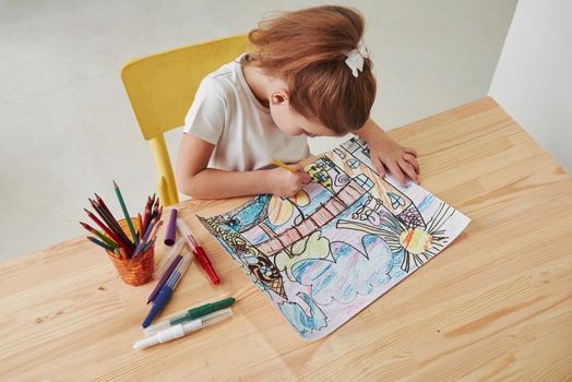 View from the top. Cute little girl in art school draws her first paintings by pencils and markers.