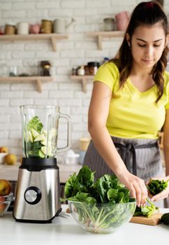 Preparing healthy foods. Healthy eating and dieting. Young brunette woman making green smoothie at home kitchen