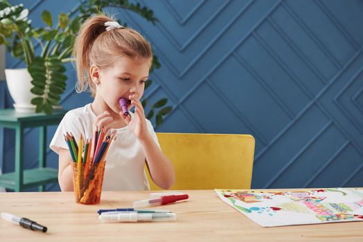 Violet marker in the mouth. Cute little girl in art school draws her first paintings.