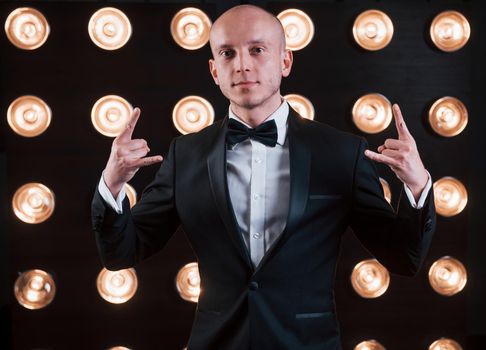 Having fun at his free time. Magician in black suit standing in the room with special lighting at backstage.