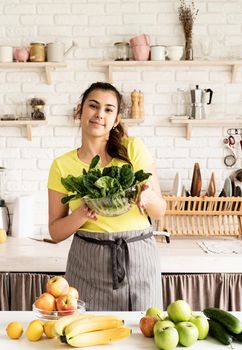 Preparing healthy foods. Healthy eating and dieting. Young caucasian brunette woman holding a bowl of fresh spinach in the kitchen