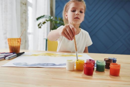 Takes the paint. Little girl is drawing by using gouache and brush. Learning in the art class.