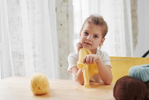 Time for the rest. Kid is knitting at home. Cute little girl sitting near the wooden table is learning some new stuff.