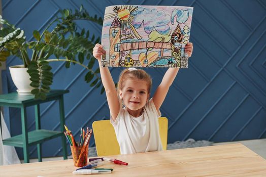 Proudly raised up her creation. Cute little girl in art school shows her first paintings drawn by pencils and markers.