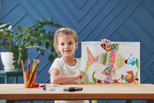 Showing off and feeling satisfaction. Cute little girl in art school shows her first paintings drawn by pencils and markers.