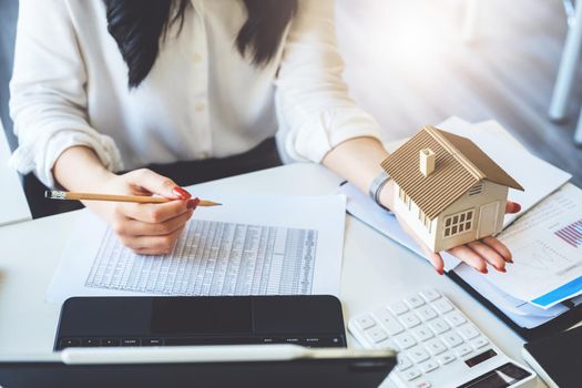 Accountant, businessman, real estate agent, Asian business woman handing model house to customers along with house interest calculation documents for customers to sign