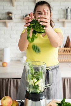 Preparing healthy foods. Healthy eating and dieting. Young brunette woman making green smoothie at home kitchen