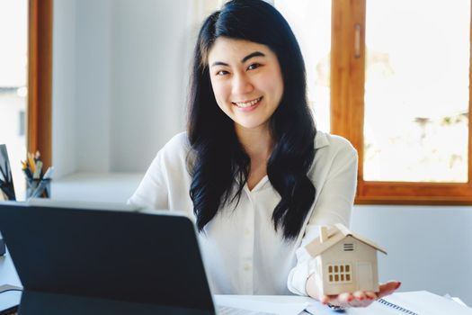 Accountant, businessman, real estate agent, Asian business woman handing model house to customers along with house interest calculation documents for customers to sign