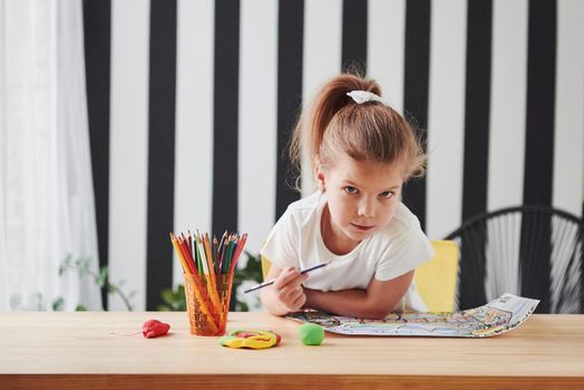 Wall with white and black stripes. Cute little girl in art school draws her first paintings by pencils and markers.