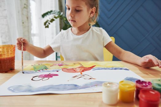 Playing with different colors. Little girl is drawing by using gouache and brush. Learning in the art class.