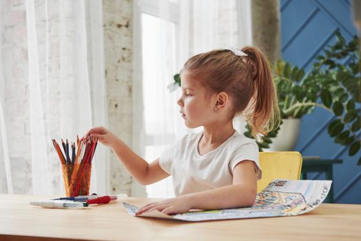 Searching for the perfect color. Cute little girl in art school draws her first paintings by pencils and markers.