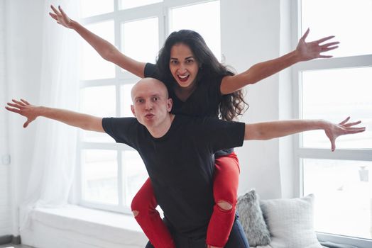 Playful couple in black and red clothes having fun in the white room in daytime.