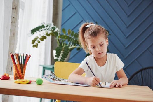 Good interior at daytime. Cute little girl in art school draws her first paintings by pencils and markers.
