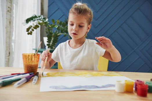 Careful movements. Little girl is drawing by using gouache and brush. Learning in the art class.