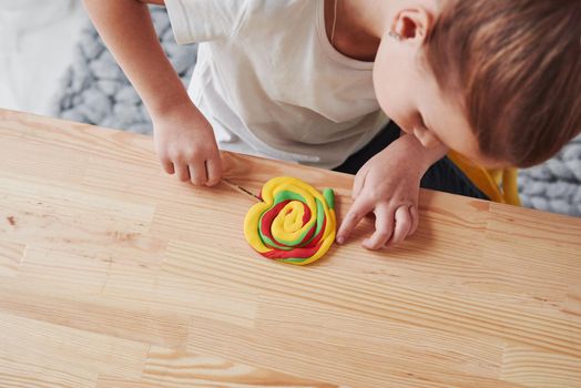 Making corrections to hand crafted artificial candy. Children playing with colored plasticine on the wooden table at home.