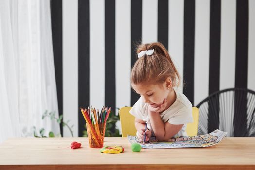 Wall with black stripes behind. Cute little girl in art school draws her first paintings by pencils and markers.