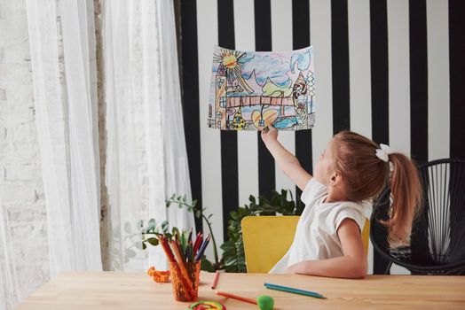 Evaluates its work. Cute little girl in art school shows her first paintings drawn by pencils and markers.