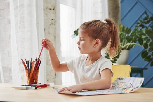 Picking pink pencil. Cute little girl in art school draws her first paintings.