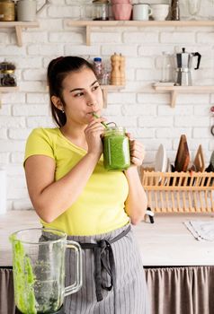 Healthy eating, dieting concept. Young brunette woman drinking green smoothie at home kitchen from mason jar
